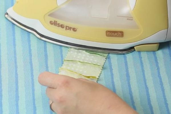 Image shows an iron pressing down a strip wrong side up of fabric on an ironing board.