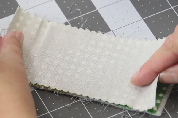 Image shows a cutting board with hands putting together fabric piece of the same size, right sides together.