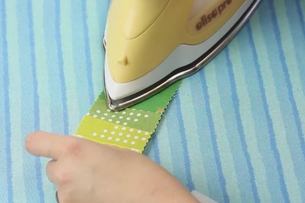 Image shows an iron pressing down a strip right side up of fabric on an ironing board.