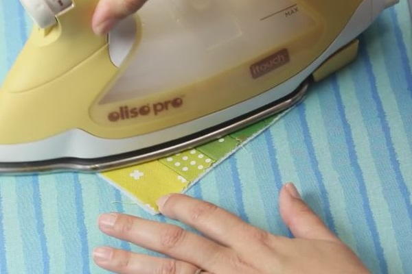 Image shows an iron pressing together the fusible fleece and strip of fabric right side up of fabric on an ironing board.