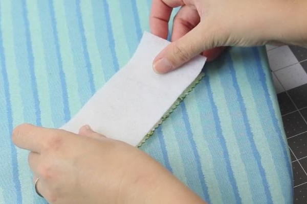 Image shows an ironing board with hands putting together the fusible fleece onto the fabric piece of the same size.