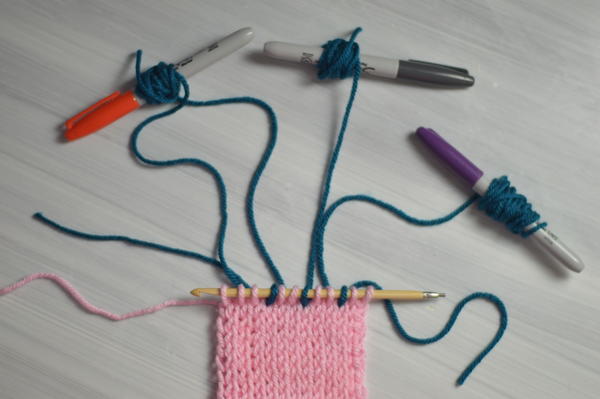 Image shows an example of markers holding the pieces of yarn being used to carry colors while Tunisian crocheting.