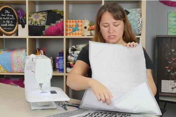 Image shows a woman at a desk with a sewing machine. She is holding the finished quilt calendar backwards, displaying the back pocket.