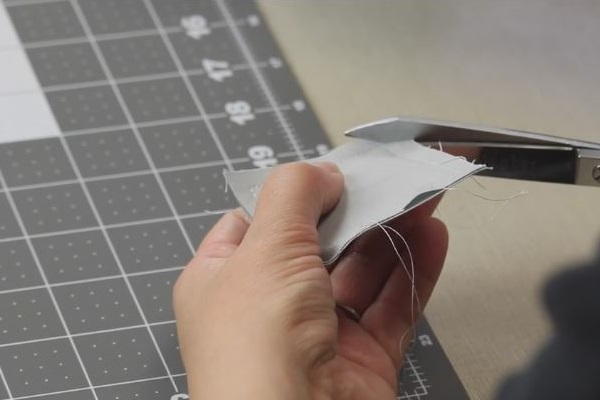 Image shows a cutting board in the background. In the foreground, a hand is holding the sewn square and is clipping a corner with scissors in the other hand.