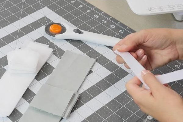 Image shows a cutting board with strips of fabric and a rotary cutter sitting on top. A hand is holding a piece of Velcro.