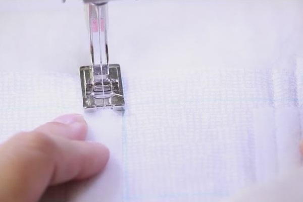 Image shows a close up of the Velcro being sewn with a machine to the piece of light fabric.