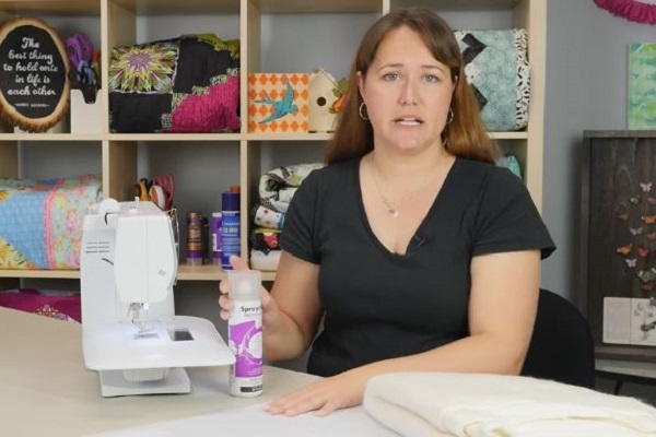 Image shows a woman at a desk with a sewing machine. She is holding basting spray.