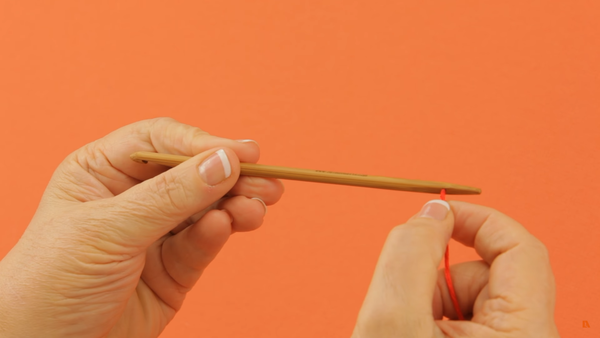 Image shows a close-up of a person's hands holding a knook tool and pushing yarn through the hole.