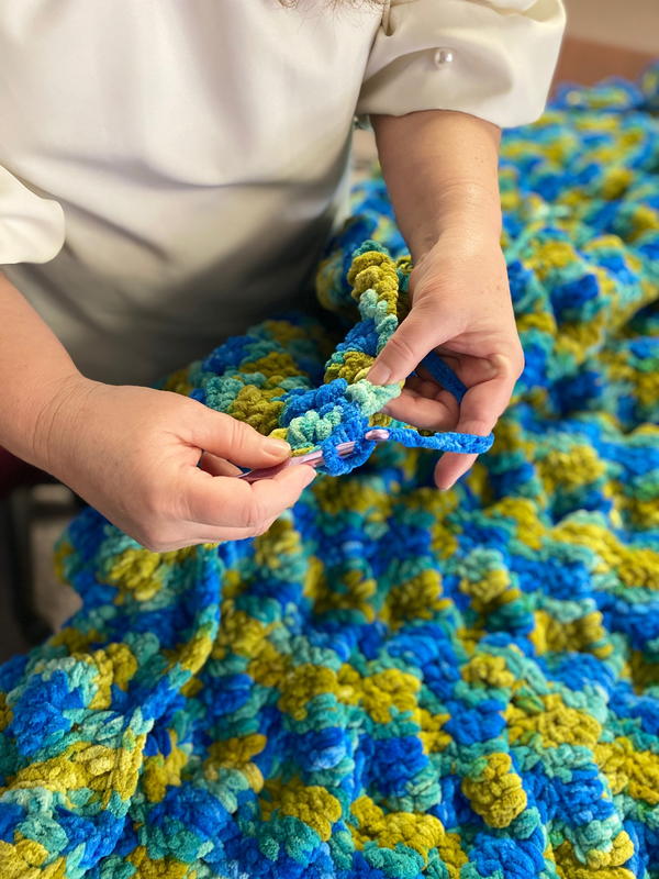 Image shows a close-up of hands crocheting a blanket that's blue and green.