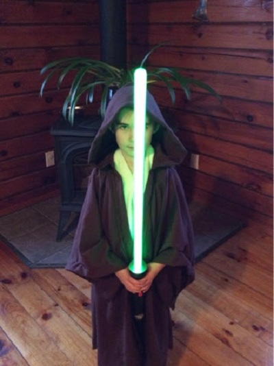 Image shows a child standing in a wood-paneled and floor room wearing the DIY Star Wars-Inspired Jedi Costume.