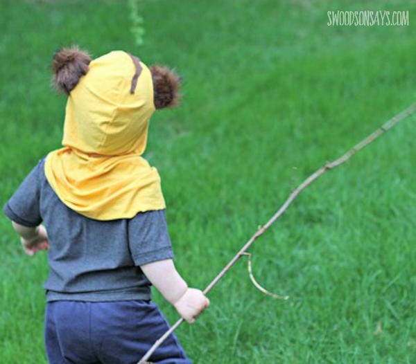 Image shows a child standing in grass wearing the Ewok Toddler Halloween Costume and holding a stick.