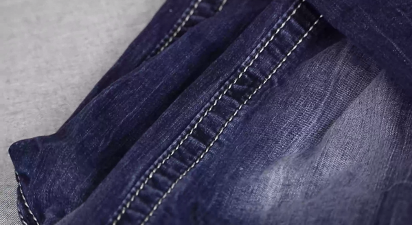 Image shows a close-up of a pair of jeans with white straight stitching on the leg.
