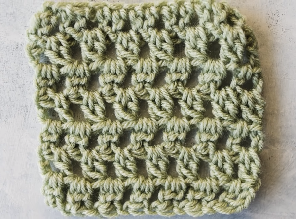 Image shows a 2 double crochet cluster stitch swatch on a gray background in a sage green yarn.
