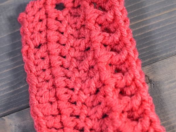 Image shows a pink Front Post Double Crochet Stitch swatch turned sideways on a gray wood background.
