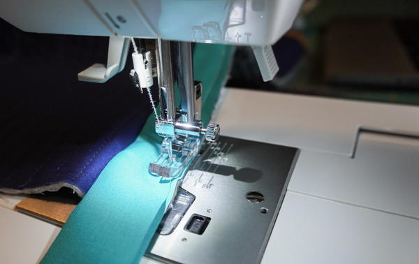 Image shows a close-up of a sewing machine binding a quilt.