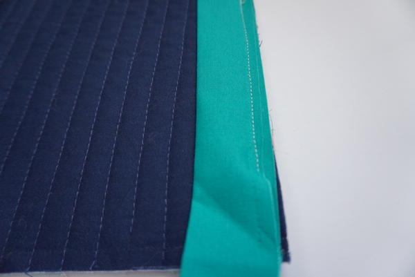 Image shows a close-up of the navy and teal quilt with wavy binding.