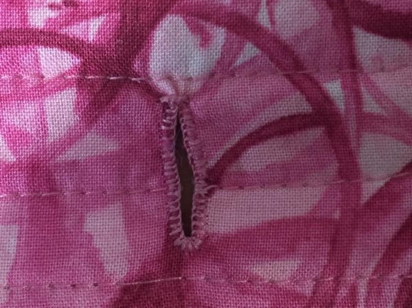 Image shows close-up of a machine buttonhole on a pink patterned sleeve.
