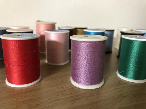 Image shows various spools of thread in different colors standing up on a wood table.