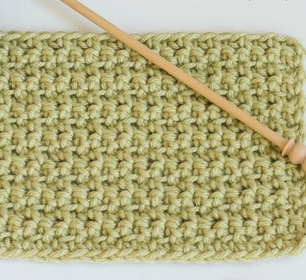 Image shows a sage green swatch made of back and front single crochet stitch. There's a light wood crochet hook sitting on top.