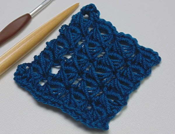 Image shows a navy swatch made using the broomstick lace crochet stitch. There's a crochet hook and knitting needle to the left of the swatch.
