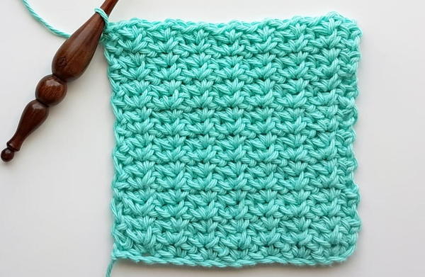 Image shows a crochet hook attached to a swatch of teal yarn made using the spider stitch.