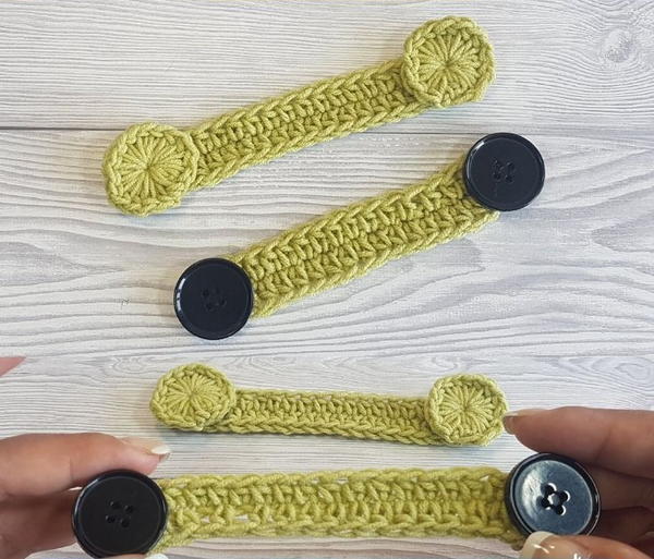 Image shows a wood background with four ear protectors in yellow. Two have crocheted yellow circles on the ends and two have black buttons on the ends. hands are holding one of the pieces.