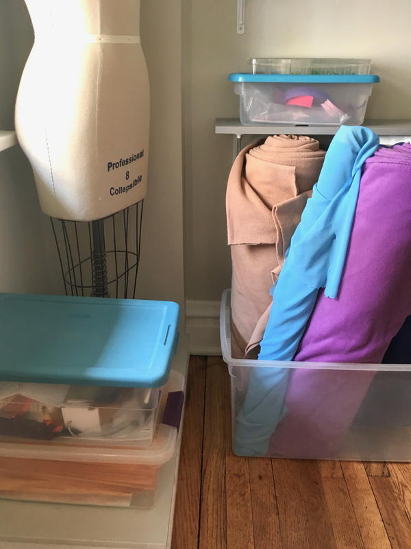 Image shows a corner in a sewing room. There is a body form and clear tubs full of sewing materials and fabric.