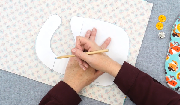 Image shows a person marking a paper template on a piece of fabric.