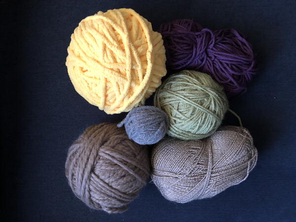 Image shows six balls of yarn in different colors and sizes on a dark background.