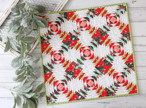 Image shows a Christmas-colored mini quilt with greenery on the side.