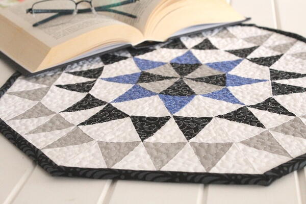 Image shows a octagonal quilt with a book laying on the edge of one side. 