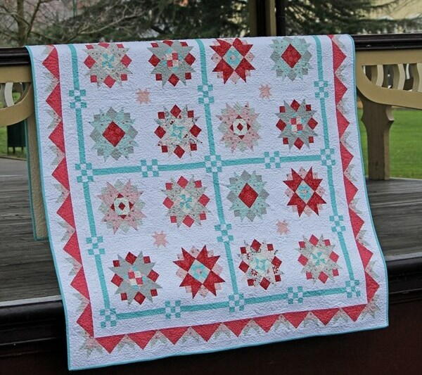 Image shows a quilt laid across a deck railing outside.