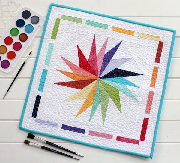 Image shows a colorful mini quilt with a paint set.