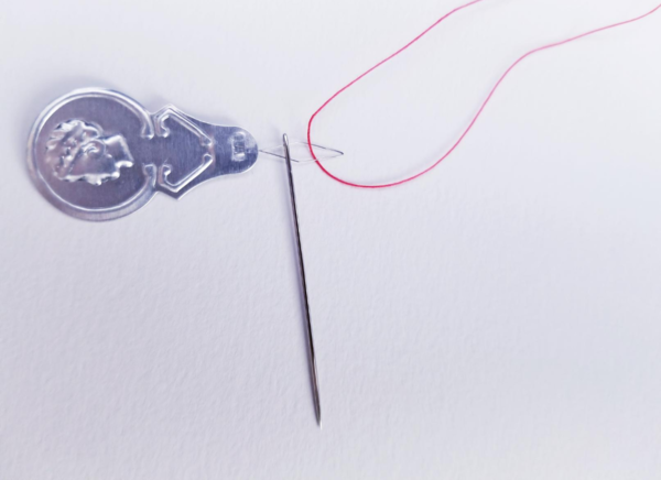 Image shows a needle pushed onto a needle threader and red thread pulled through the loop on a light background.