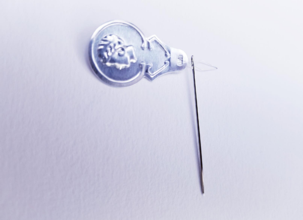 Image shows a needle pushed onto a needle threader on a light background.