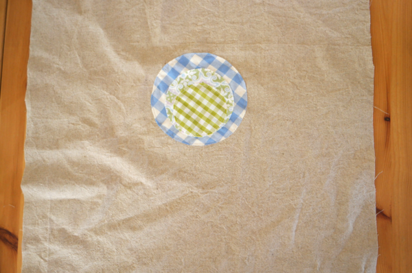 Image shows circle fabric flower piece sewn on the main bag piece, sitting on a wood table.