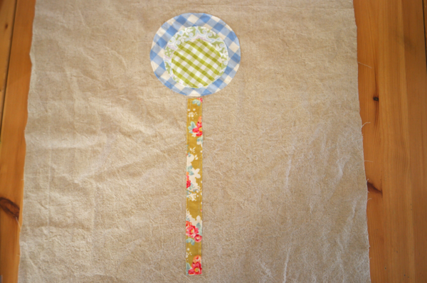 Image shows circle fabric flower and stem pieces sewn on the main bag piece, sitting on a wood table.