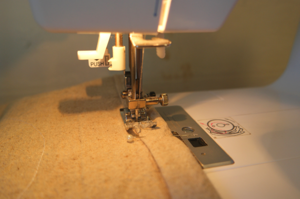 Image shows a close-up of a sewing machine sewing the hem for the top edge of the bag.