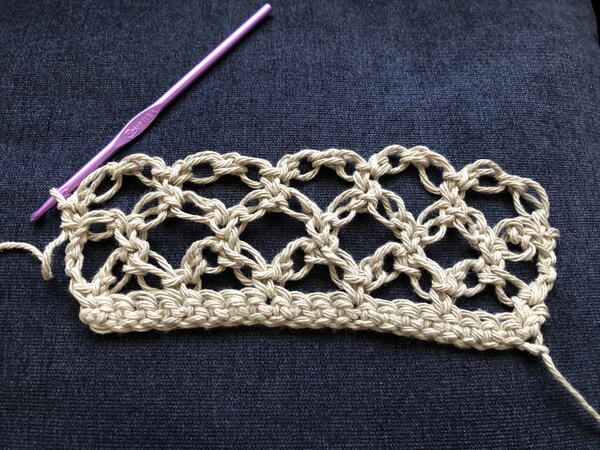 Image shows a crochet Solomon's Knot sample with a crochet hook still attached.