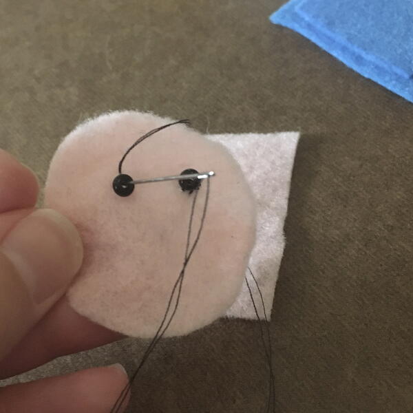 Image shows sewing seed bead eyes on the felt face circle for the DIY Gnome Ornament.