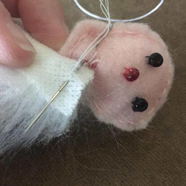 Image shows sewing the white faux fur fabric beard pieces to face for the DIY Gnome Ornament.