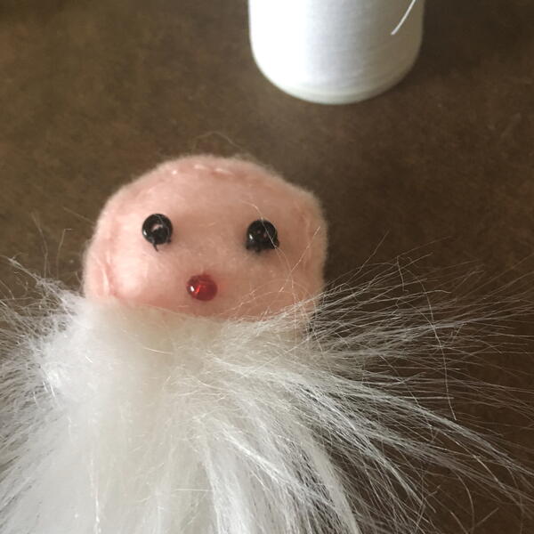 Image shows the white faux fur fabric beard sewn to the face for the DIY Gnome Ornament.