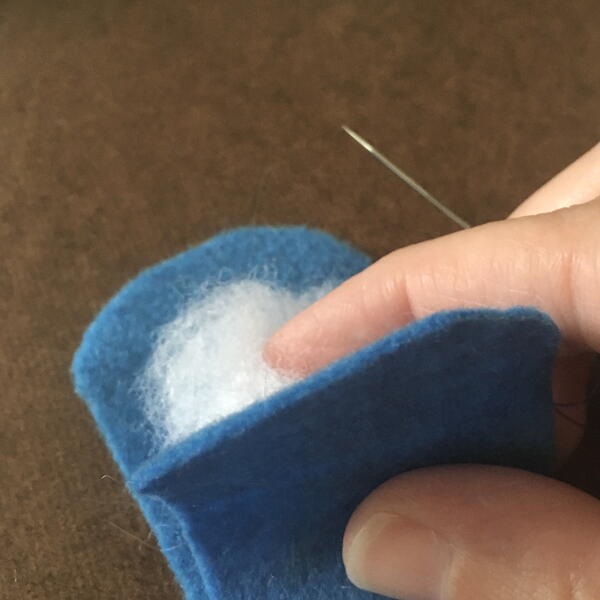 Image shows the blue felt body pieces being stuffed for the DIY Gnome Ornament.