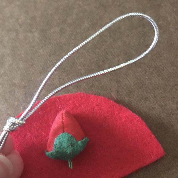Image shows a half-circle of red felt, a pincushion strawberry, and silver string for the DIY Gnome Ornament.