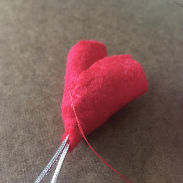Image shows the half-circle of red felt wrapped around the pincushion strawberry and silver string for the DIY Gnome Ornament.