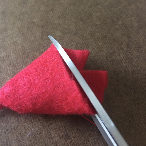 Image shows the half-circle of red felt hat being trimmed flat for the DIY Gnome Ornament.