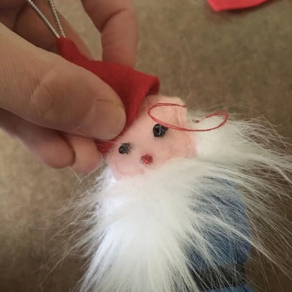Image shows the red hat being attached to the head for the DIY Gnome Ornament.