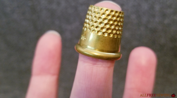 Image shows an open top thimble on a finger.