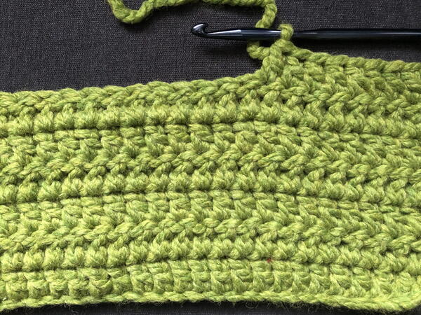 Image shows the start of a double crochet stitch blanket in green.
