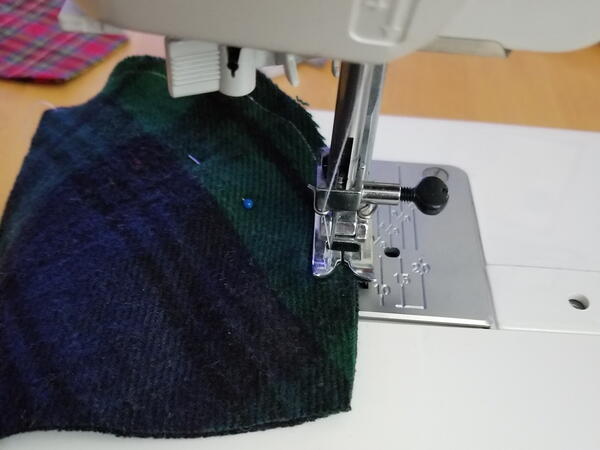 Image shows a sewing machine sewing the curved edge of the DIY mask.